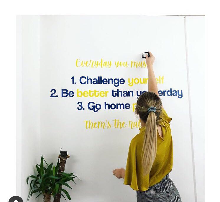 Person sticking motivational quotes on a wall with a plant beside them.