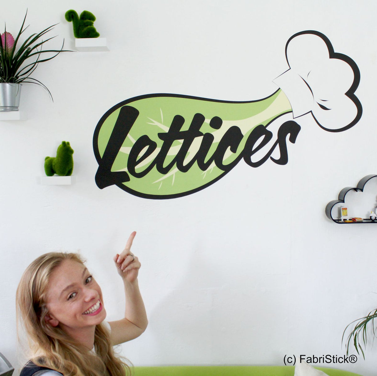 Woman pointing at a decorative wall sign with 'Lettices' and a lettuce illustration.