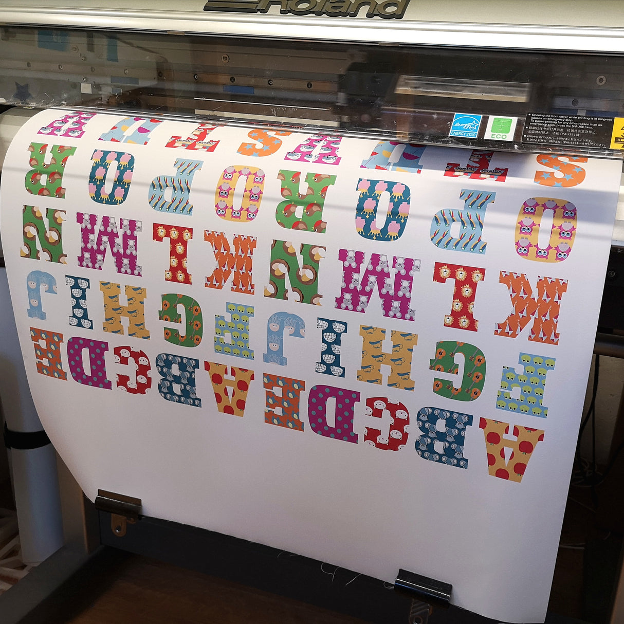Colorful lettering on a roll of paper being printed by a large printer.