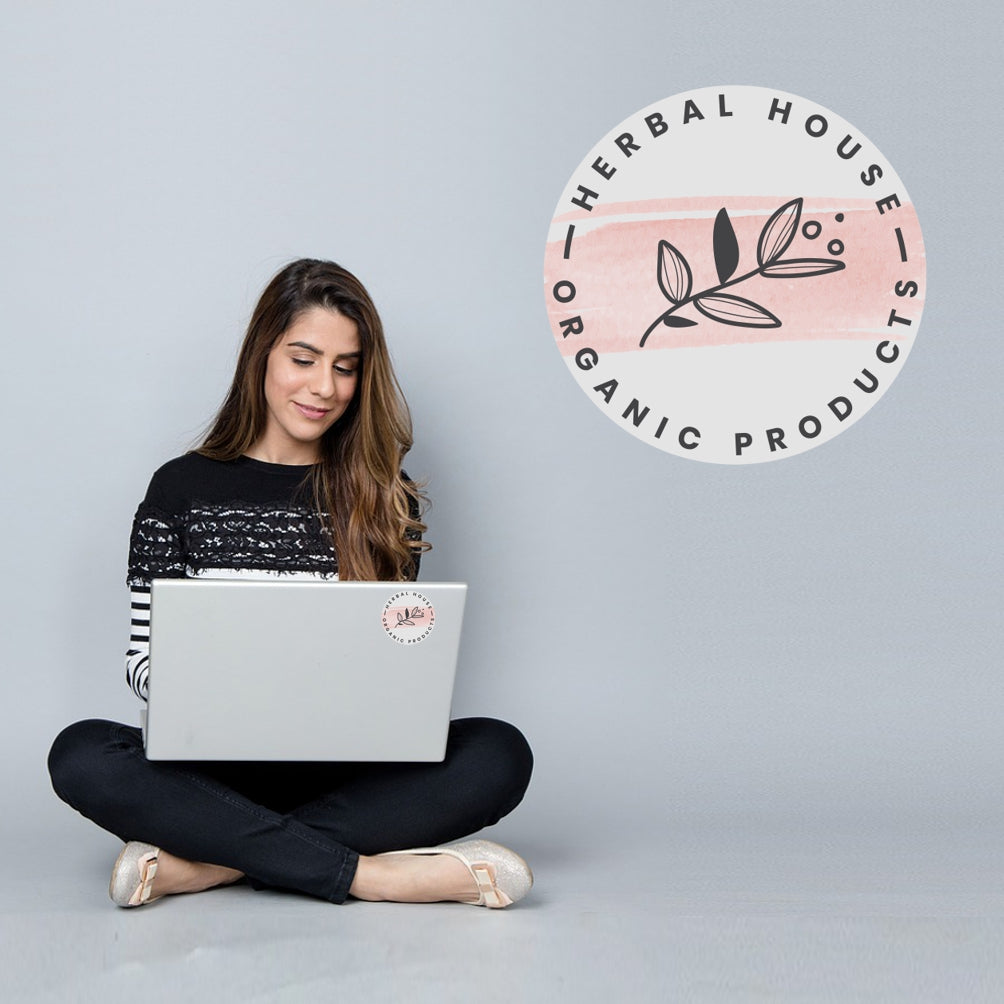 Woman sitting cross-legged using a laptop with 'Herbal House Organic Products' logo in the corner.
