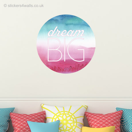 Decorative wall sticker with 'dream BIG' text on a colorful gradient background, above a bed with patterned pillows.
