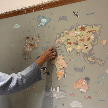 Hand placing a sticker on a world map mural on a wall.