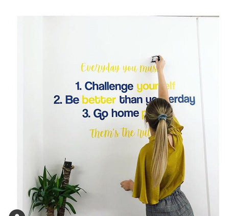 Person sticking motivational quotes on a wall with a plant beside them.