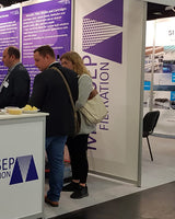 People interacting at a trade show booth with a prominent display of text and branding.