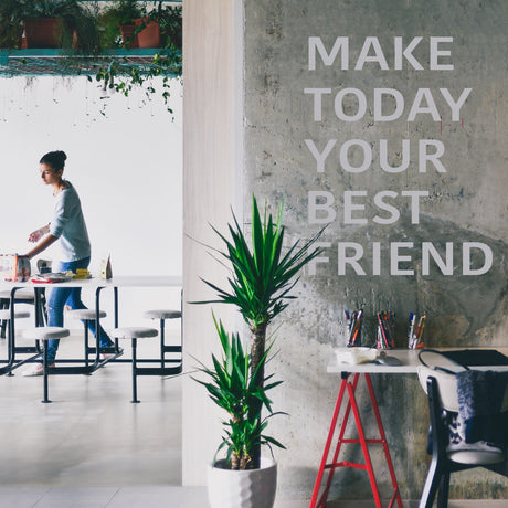 Modern interior with a person working at a desk, plants, and motivational quote on a wall.