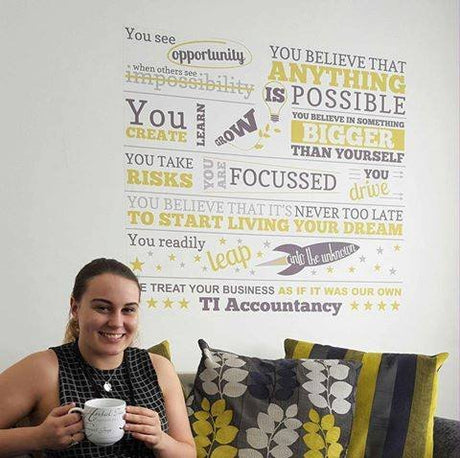 Woman holding a mug in front of a wall with motivational quotes and 'TI Accountancy' branding.