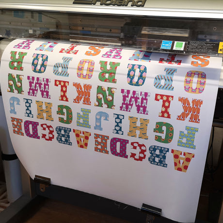 Colorful lettering on a roll of paper being printed by a large printer.