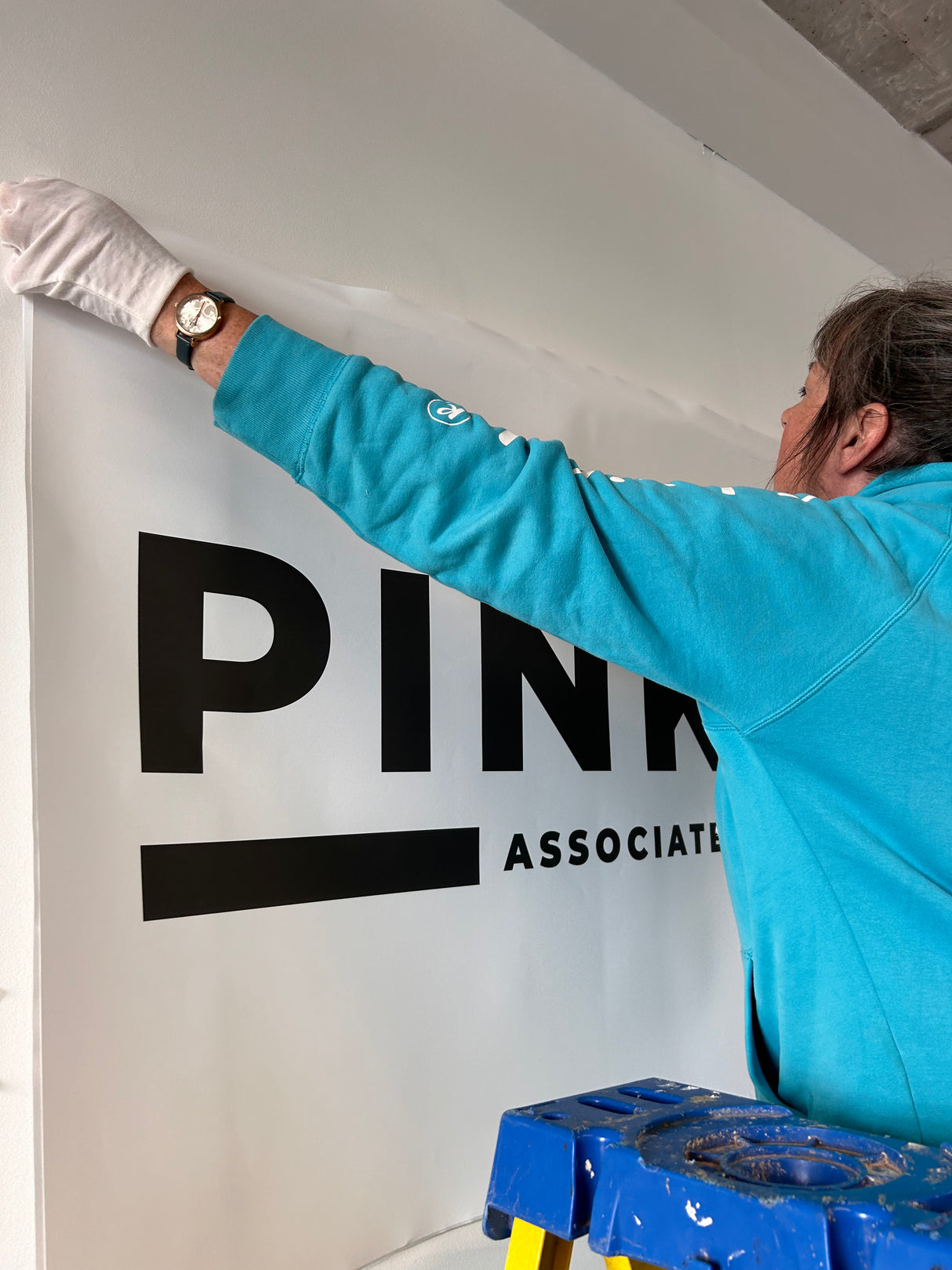 Person in a blue shirt applying a 'PINK' sign to a wall.