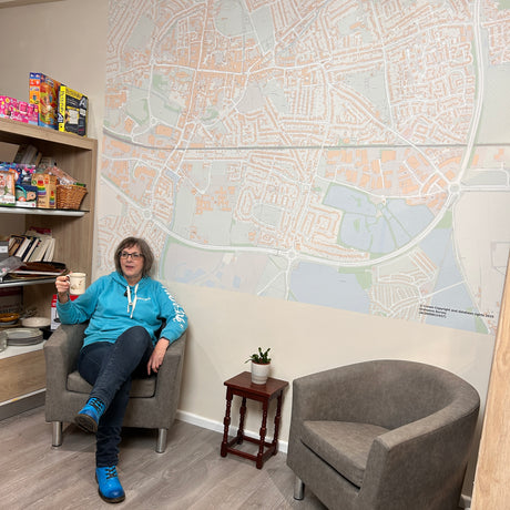 Person sitting in a chair holding a cup in front of a large wall map